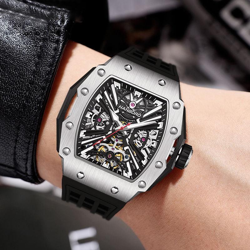 Luxury sport-inspired skeleton watch with tonneau-shaped silver case and black strap on wrist