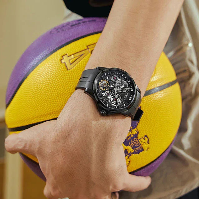 Luxury sport-inspired skeleton watch with black strap on wrist holding yellow basketball